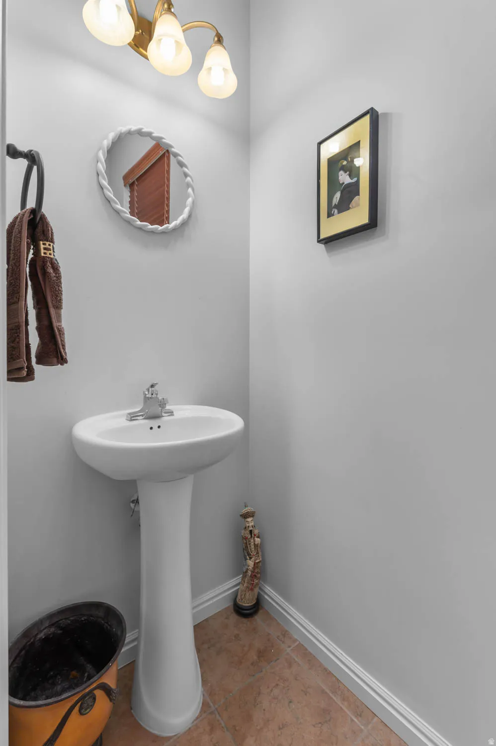 Pedestal sink with chrome faucet, complemented by a decorative mirror and sconce lighting