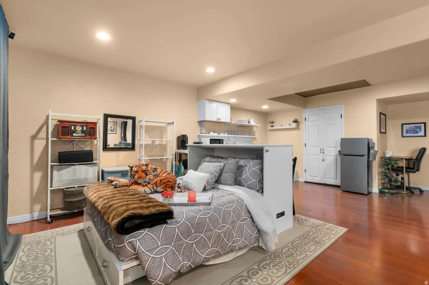 Spacious multi-purpose room featuring wood-finish flooring, recessed lighting, and a built-in kitchen area with white cabinetry