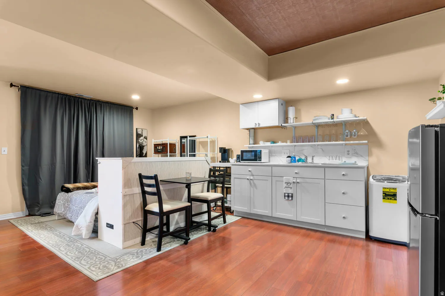 Open-concept living area with wood-finish flooring, a contemporary kitchenette featuring white cabinetry, a marble-look backsplash, and integrated shelving