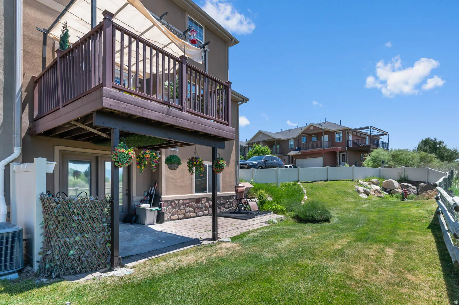 Upper-level deck with dark wood railing and a lower-level patio featuring stone accents