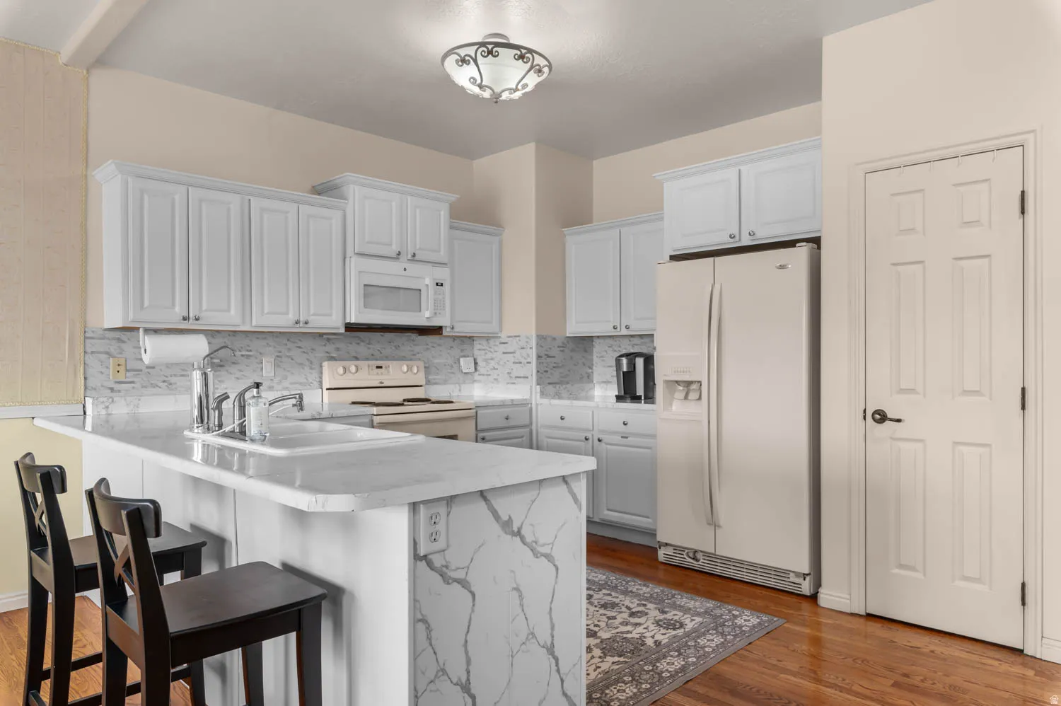 Kitchen featuring white shaker-style cabinetry, a white subway tile backsplash, and light-toned countertops with a waterfall edge