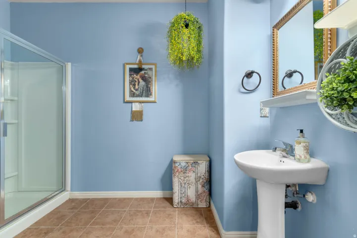 Pedestal sink with chrome faucet, framed mirror, and a walk-in shower with clear glass enclosure