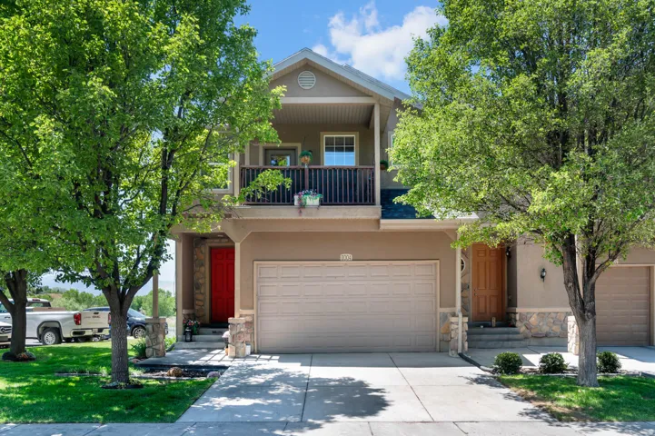 Two-story residence featuring a beige stucco exterior with stone accents, an attached two-car garage, and a second-story balcony with dark railings