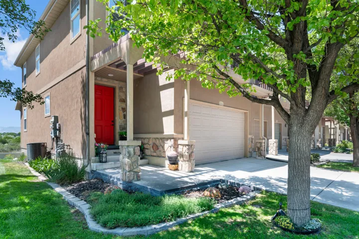 Stucco exterior with stone accents, featuring a bright red entry door, a covered porch, and an attached garage