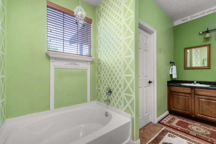 White soaking tub with decorative window surround, light green walls, and decorative geometric wall pattern