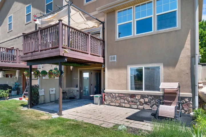 Rear exterior featuring a multi-level deck with dark wood railing, a ground-level patio with paver stones, and a stucco facade with stone accents