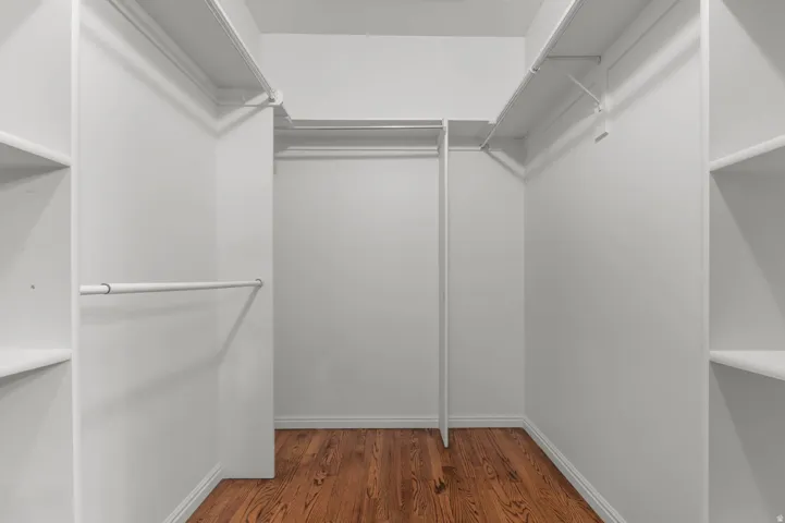 Walk-in closet featuring wood-finish flooring, white walls, and built-in shelving