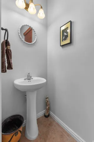 Pedestal sink with chrome faucet, complemented by a decorative mirror and sconce lighting