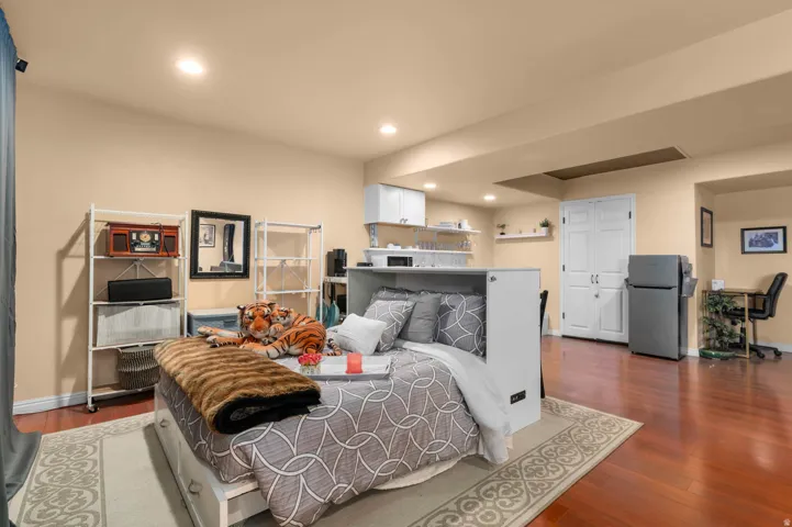 Spacious multi-purpose room featuring wood-finish flooring, recessed lighting, and a built-in kitchen area with white cabinetry