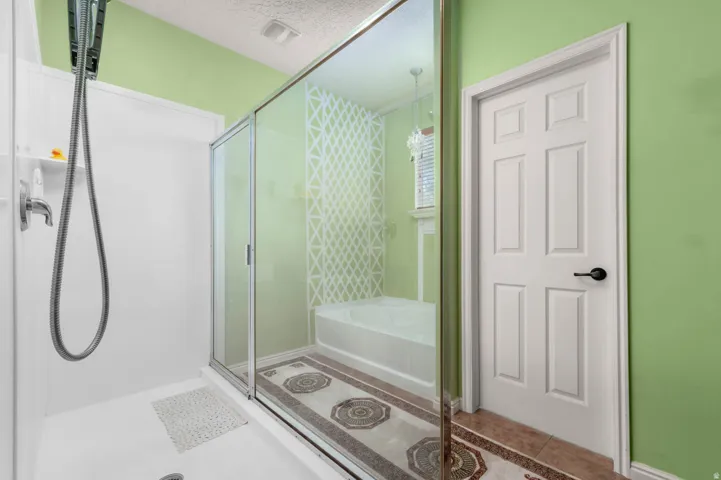 Shower stall with handheld showerhead, glass-enclosed bathtub, decorative floor tiles, and a six-panel interior door with black hardware