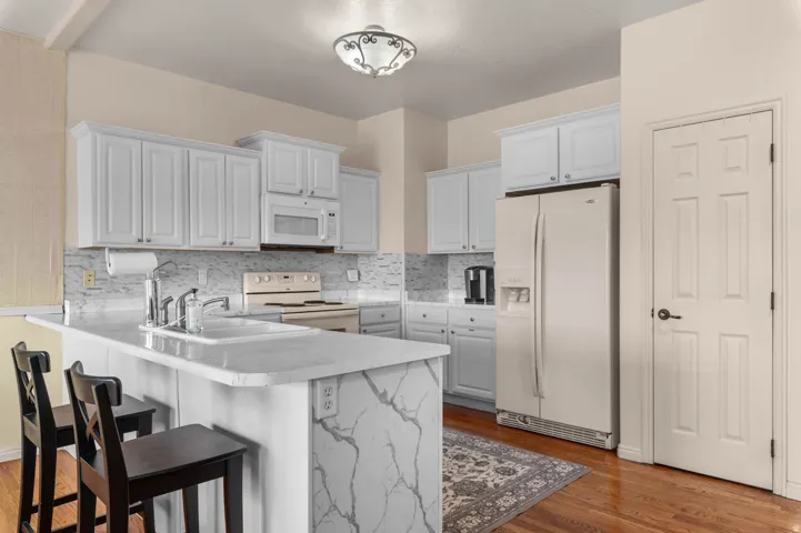 Kitchen featuring white shaker-style cabinetry, a white subway tile backsplash, and light-toned countertops with a waterfall edge