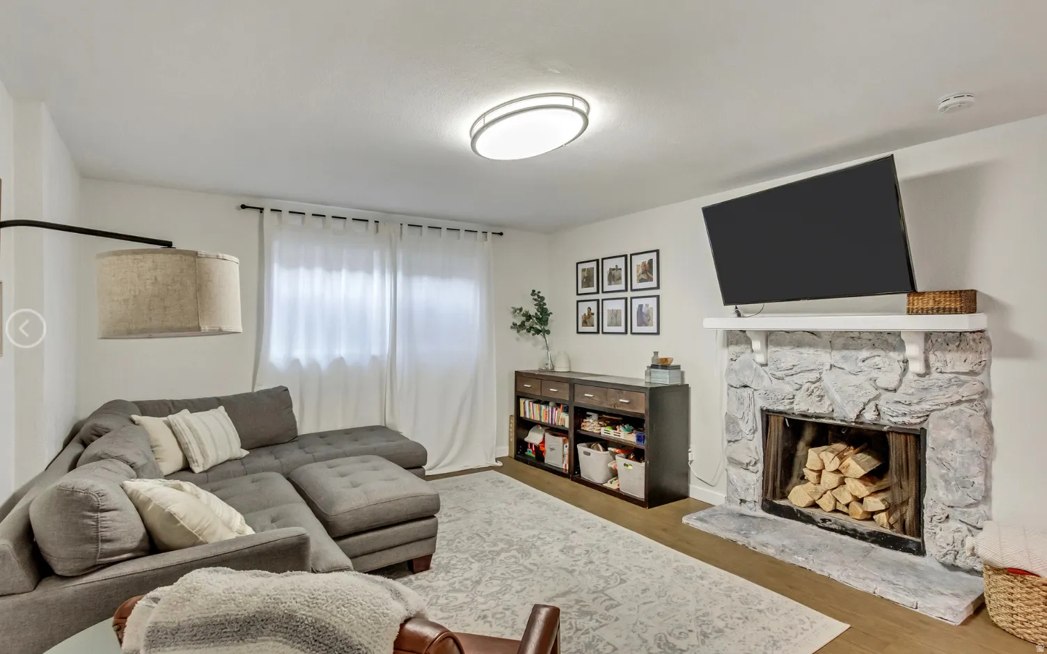 Living area featuring a stone-clad fireplace with a hearth, wood-finish flooring, and white walls