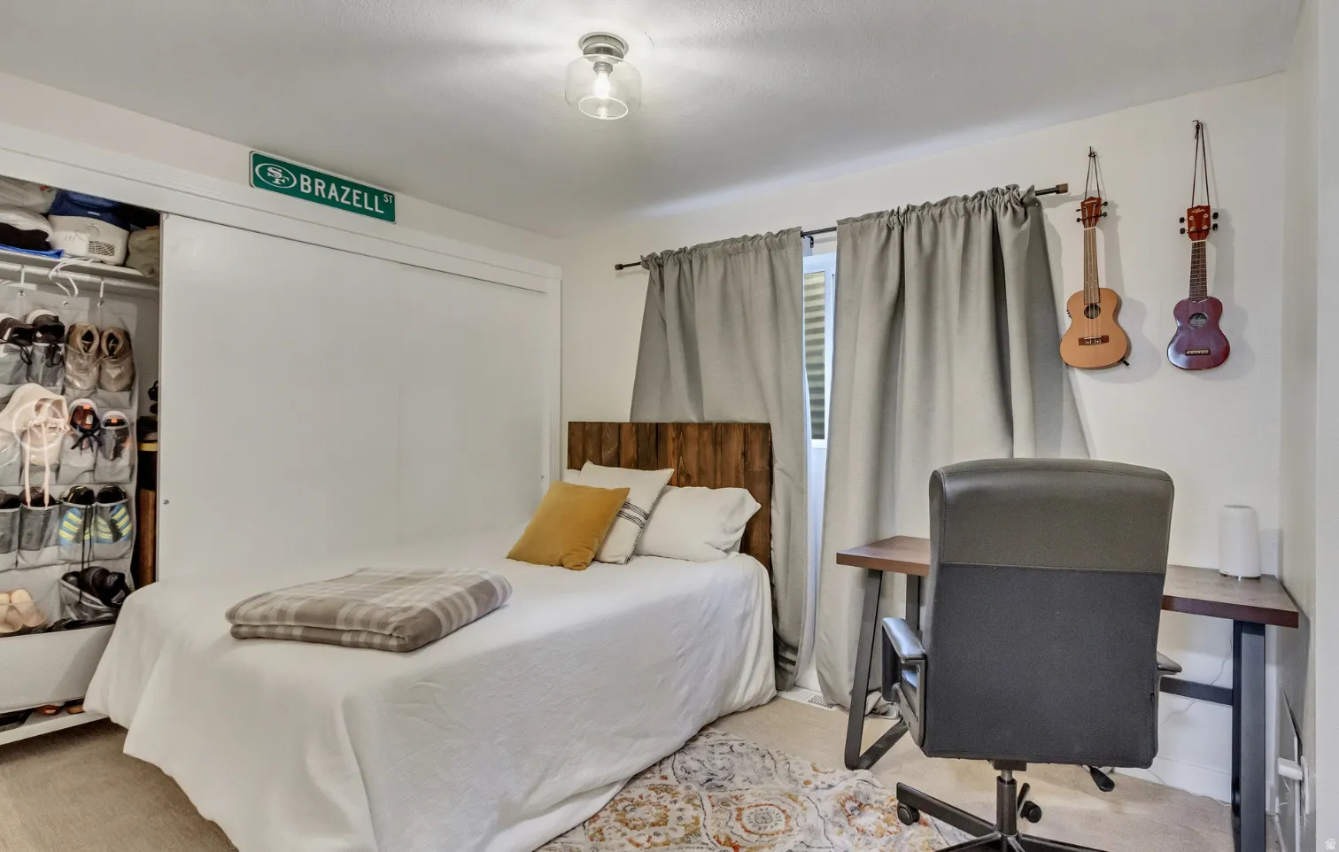 Bedroom featuring a sliding closet door, wood-finish headboard, window with privacy blinds and drapes, light-toned flooring, and a flush mount ceiling light