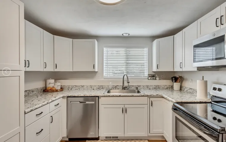 Kitchen featuring white shaker-style cabinetry with matte black hardware, granite countertops, and stainless steel appliances including a dishwasher, microwave, and range