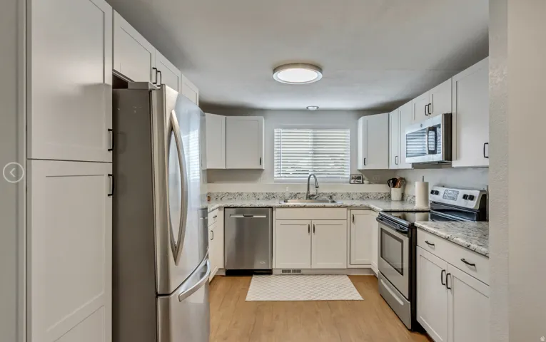 Kitchen featuring white cabinetry, stainless steel appliances, speckled countertops, and wood-finish flooring