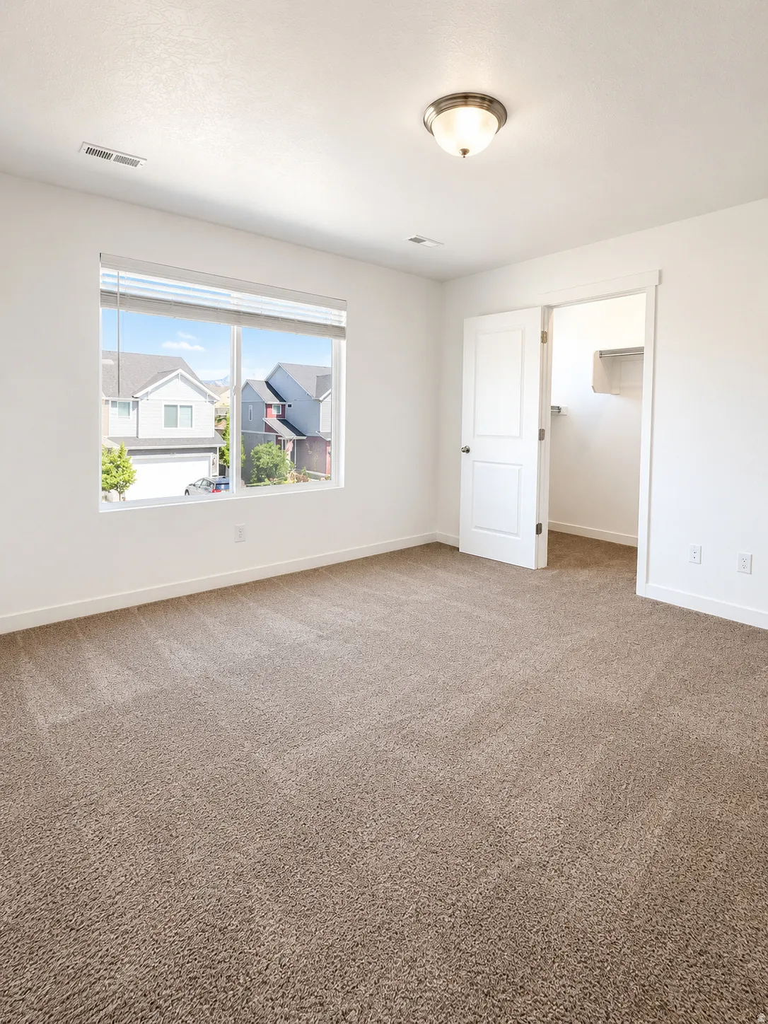 Spacious main room with plush carpeting, neutral wall finishes, and a large window providing ample natural light