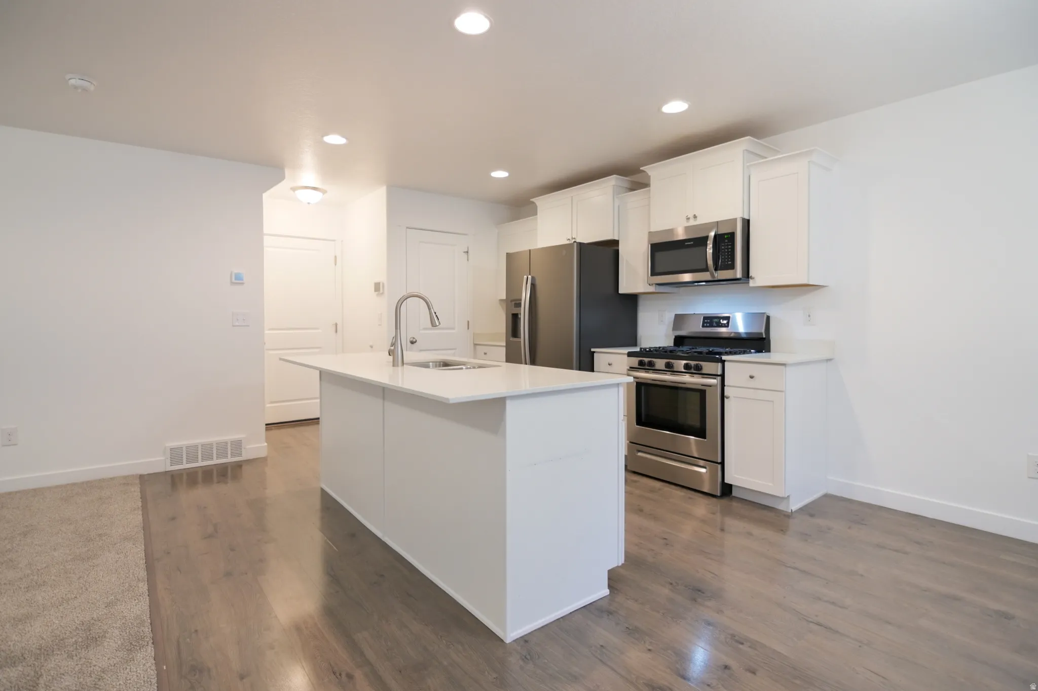 Modern kitchen featuring white cabinetry, stainless steel appliances, a center island with sink, and wood-finish flooring