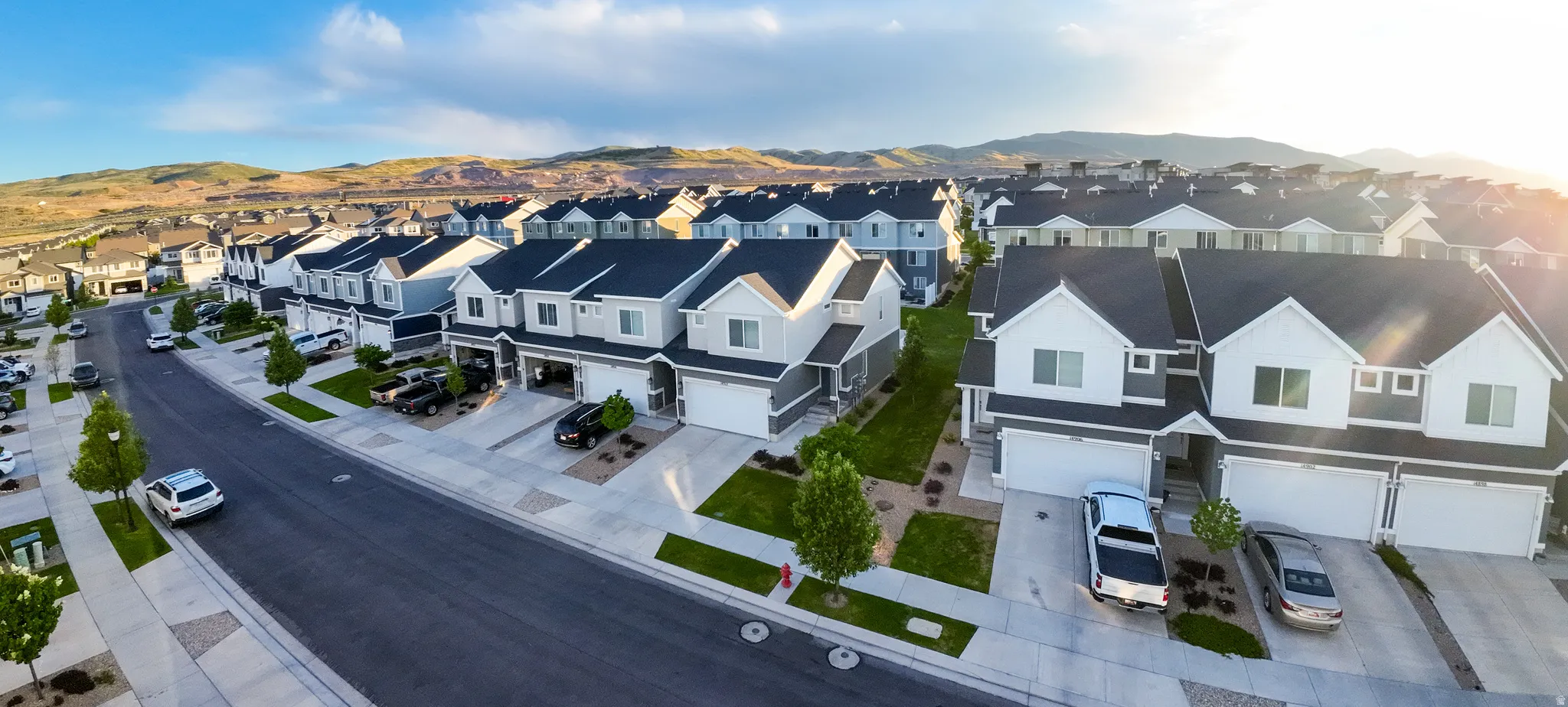 Residential streetscape featuring a collection of two-story homes with attached garages, light-toned siding, and dark roofing