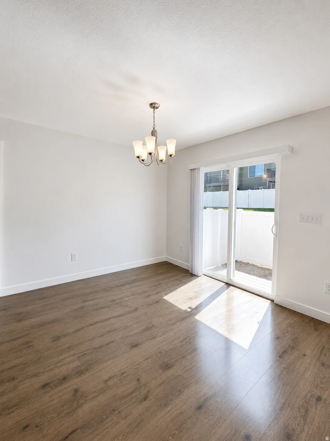 Open-concept dining are featuring wood-finish flooring, a contemporary chandelier, white walls, and a sliding glass door leading to an outdoor area