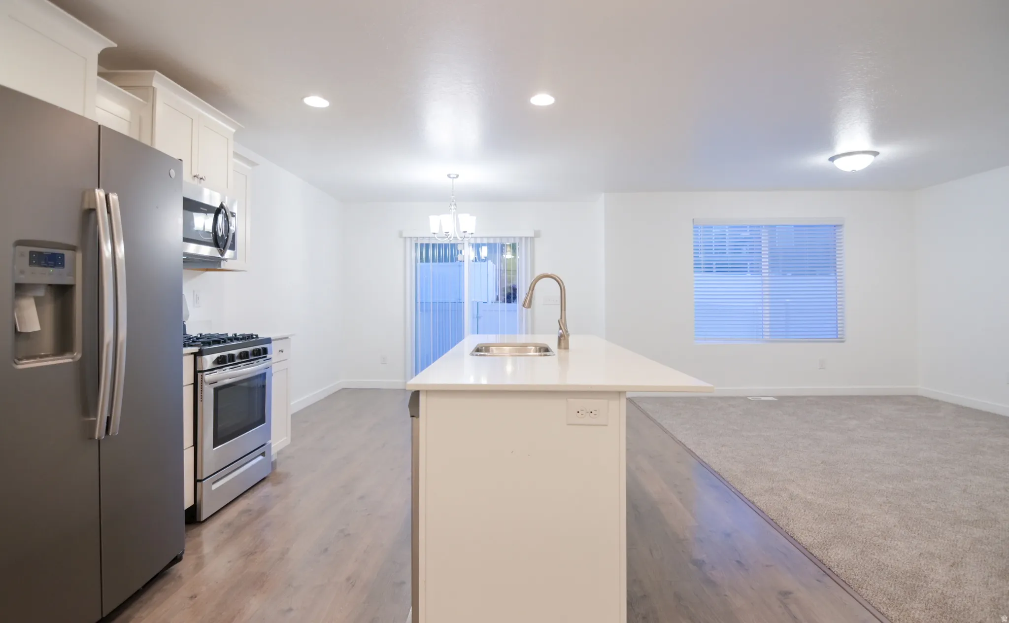 Modern kitchen featuring a large island with an undermount sink, stainless steel appliances, white cabinetry, wood-finish flooring, and recessed lighting