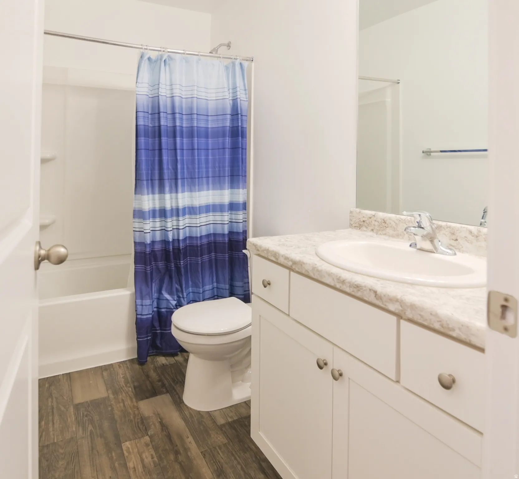 Full bathroom featuring a white vanity with an integrated sink, a light-toned countertop, and wood-finish flooring