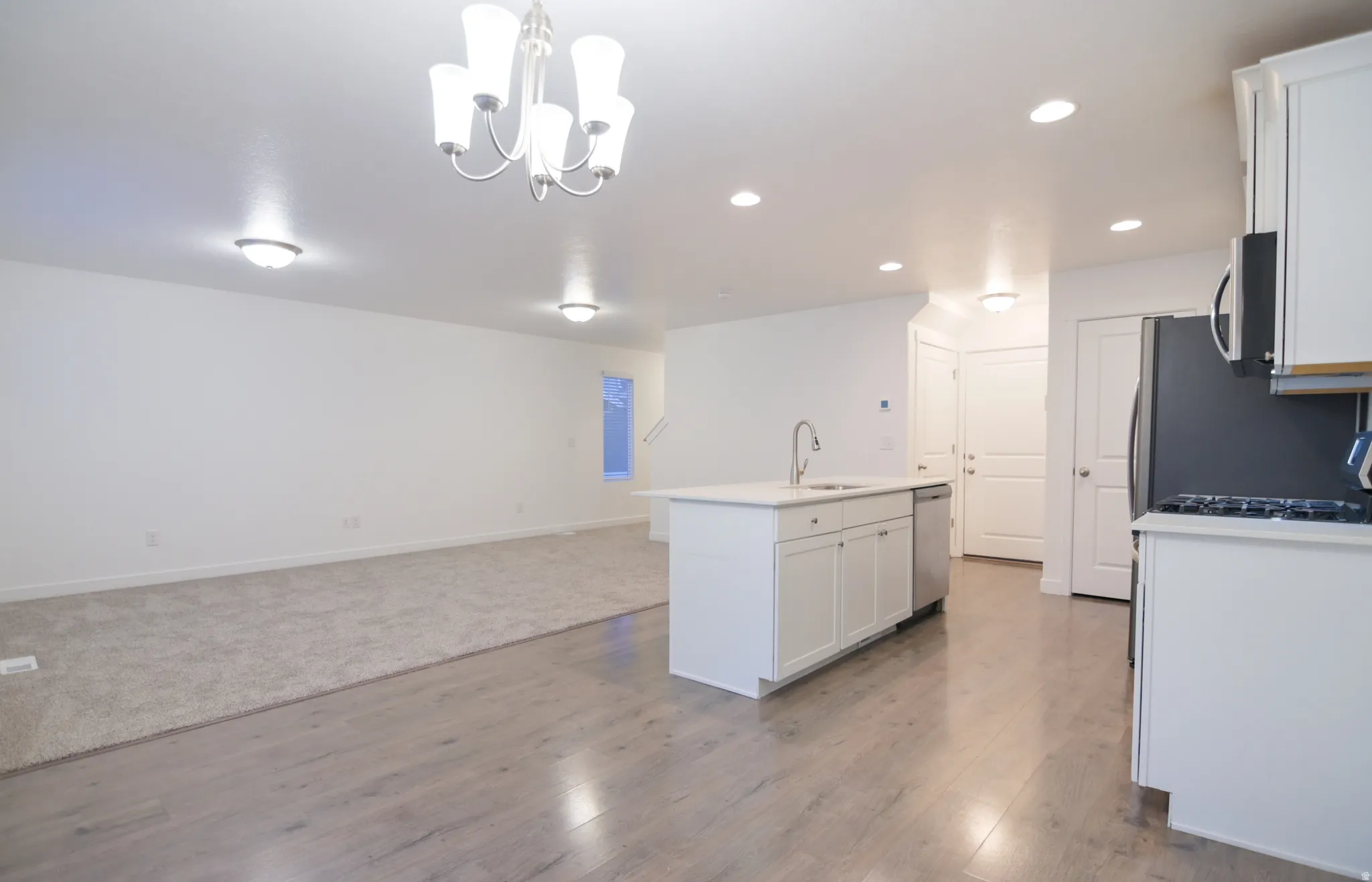 Open-concept living space featuring wood-finish flooring, a kitchen island with sink, white cabinetry, and recessed lighting