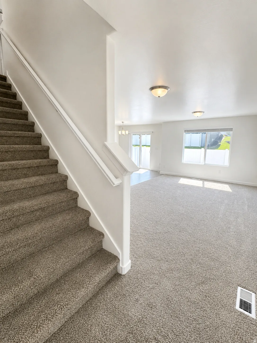 Carpeted staircase with white balustrade, opening to a spacious room with neutral carpeting and bright white walls