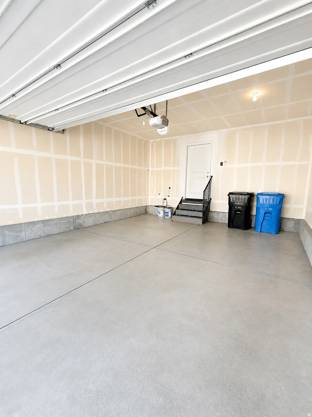 Spacious 2 car garage with concrete flooring, automatic overhead door, and a dedicated entry door