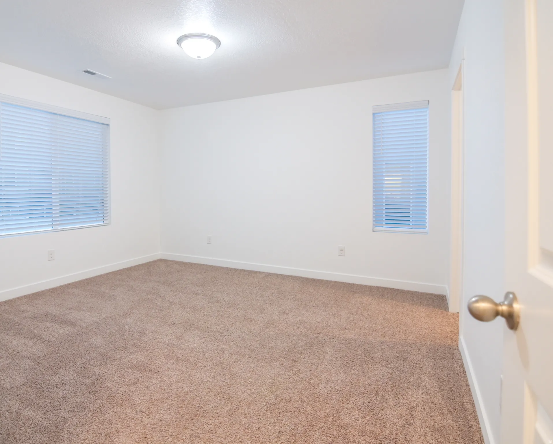 Spacious bedroom with white walls, and two windows and walk-in closet