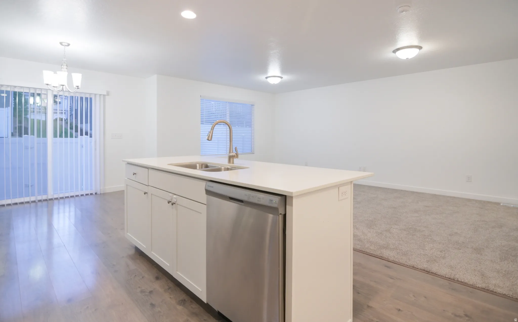 Kitchen island featuring a stainless steel dishwasher, an undermount sink with a gooseneck faucet, and white cabinetry
