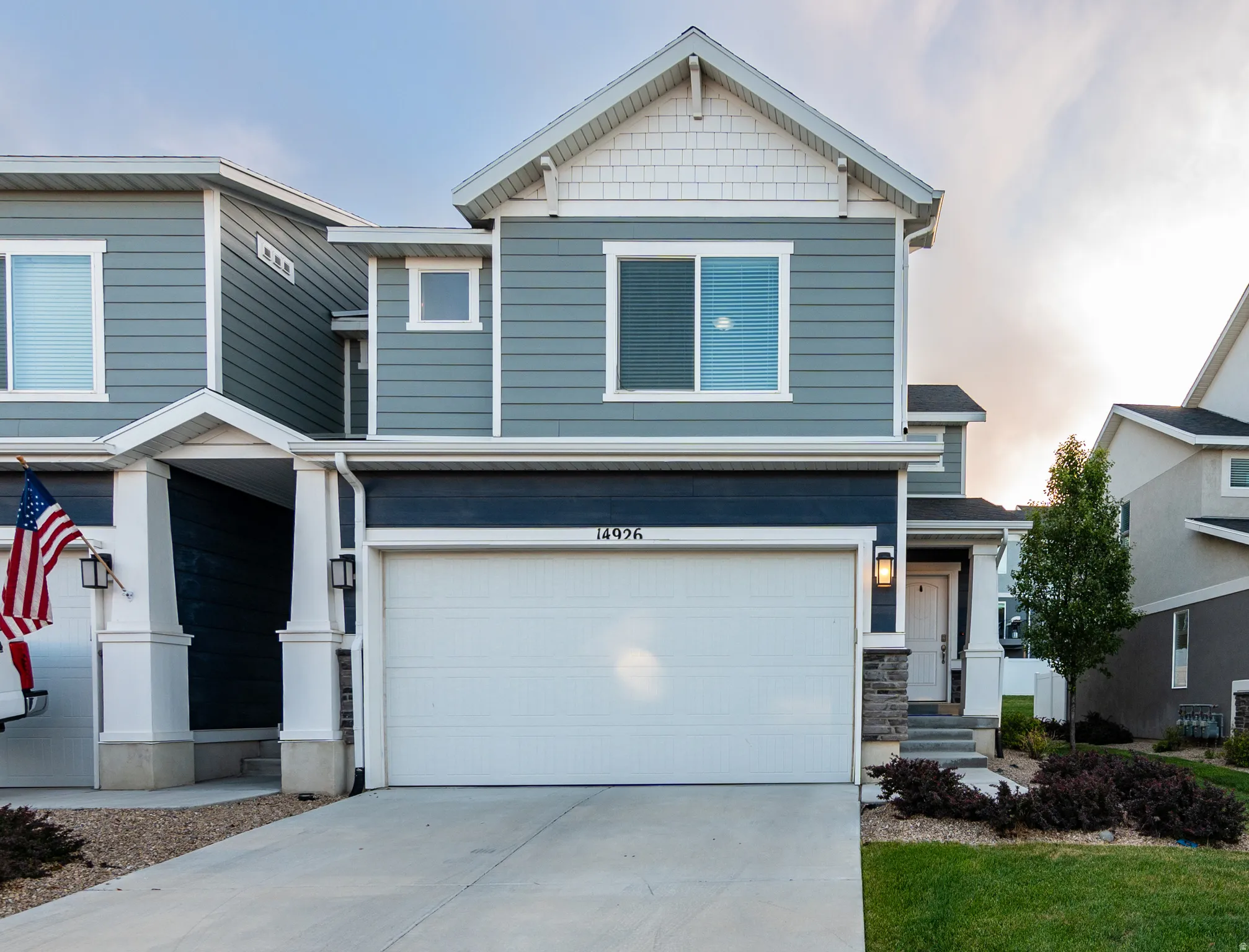 Modern two-story townhome featuring blue siding, white trim, a covered entry with columns, an integrated two-car garage, and stone accents