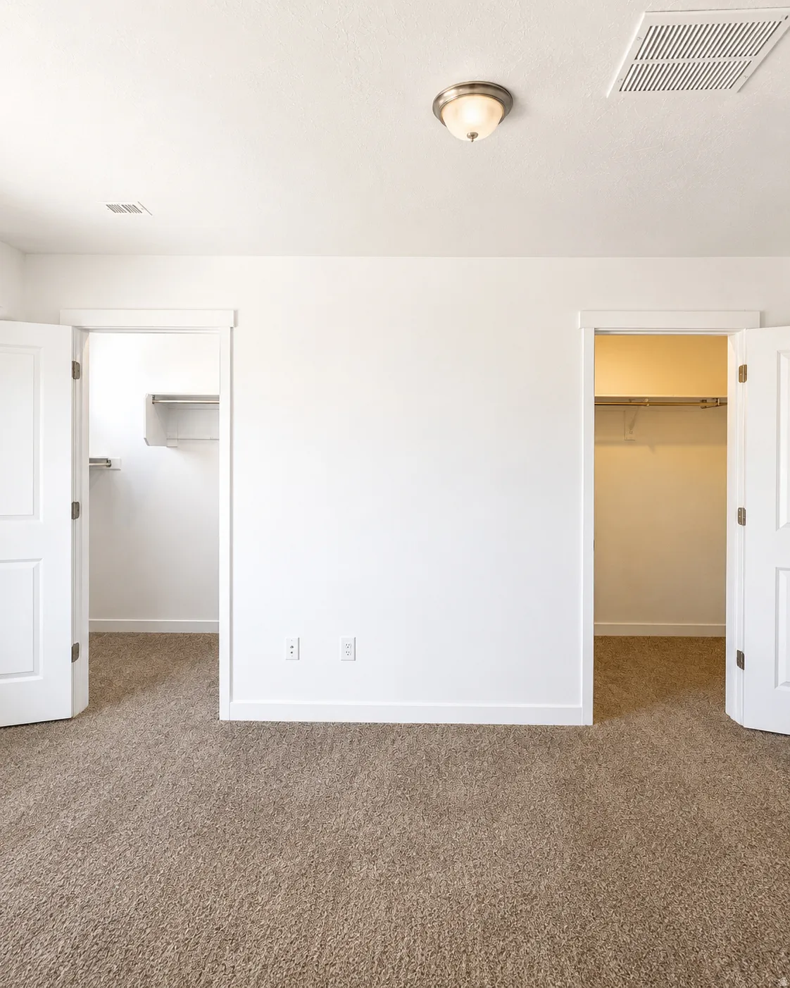 Room featuring neutral-toned carpeting, white walls, and two walk in closets