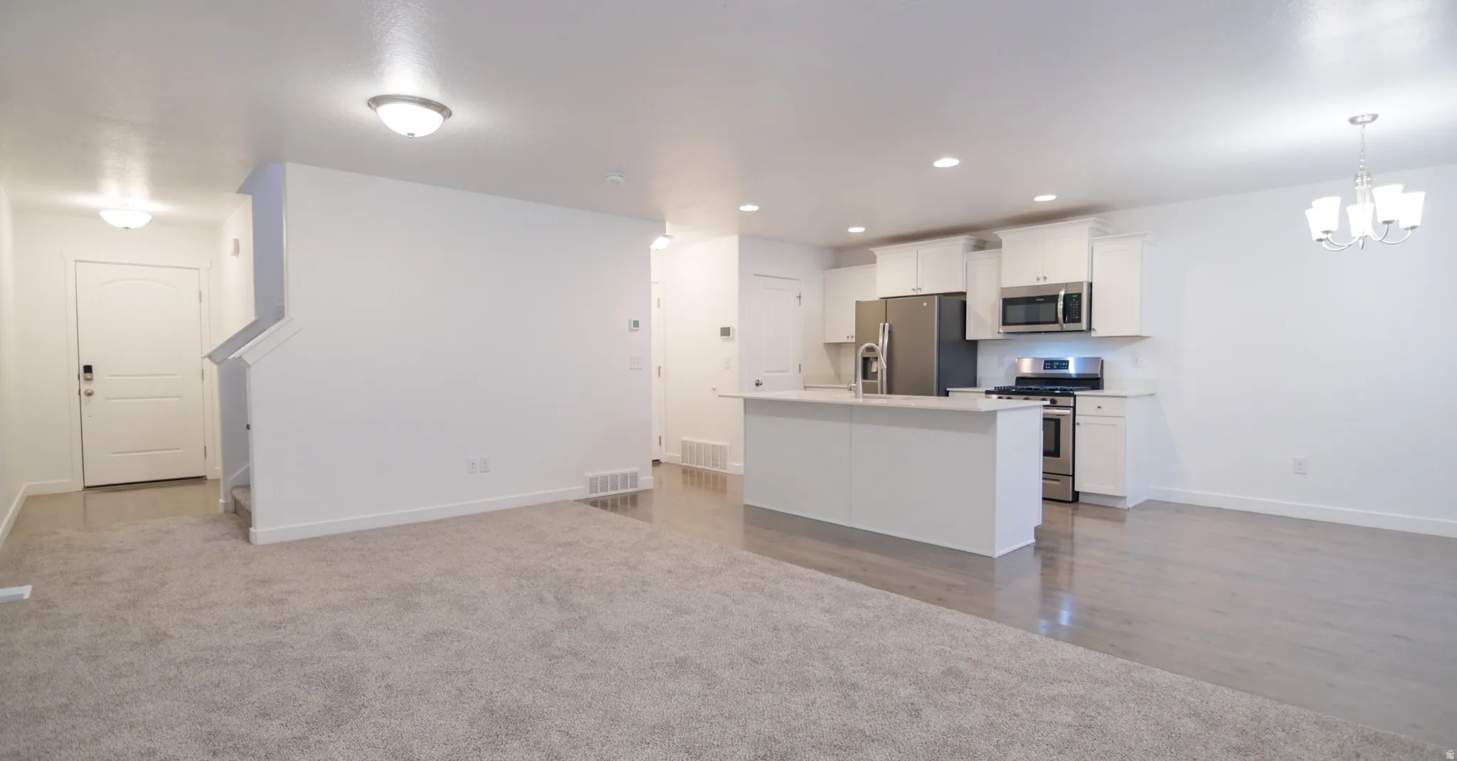 Open concept living area featuring a kitchen with white cabinetry, stainless steel appliances, and a central island with a sink