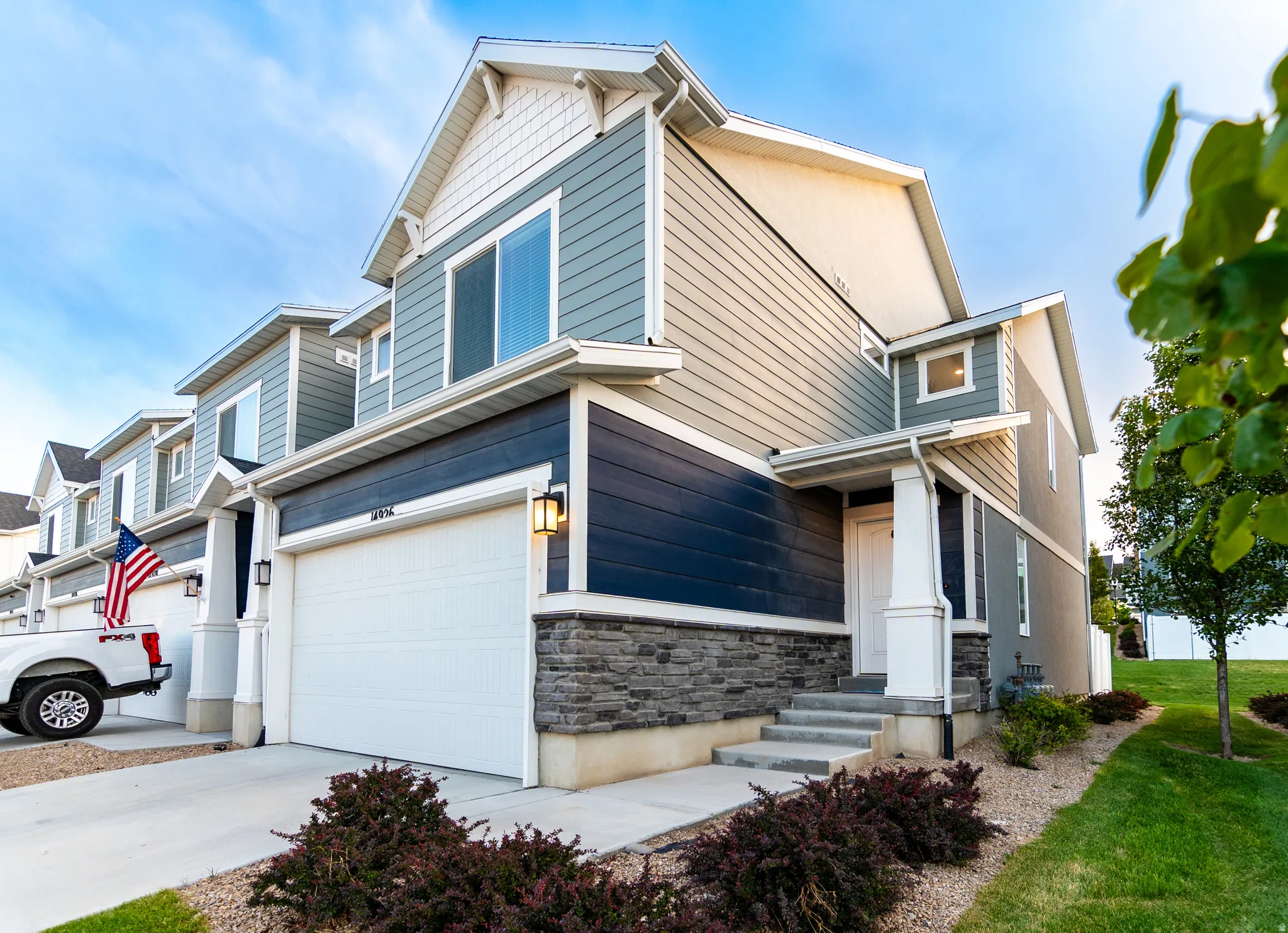 Contemporary townhome exterior featuring multi-toned siding, a stone veneer foundation, and an attached garage with an exterior light fixture