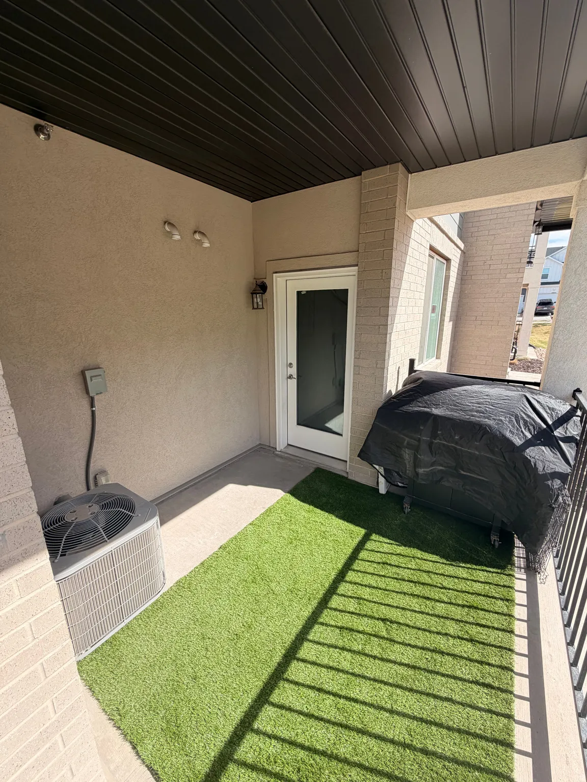 Covered outdoor patio with a black slatted ceiling, stucco walls, and a concrete floor