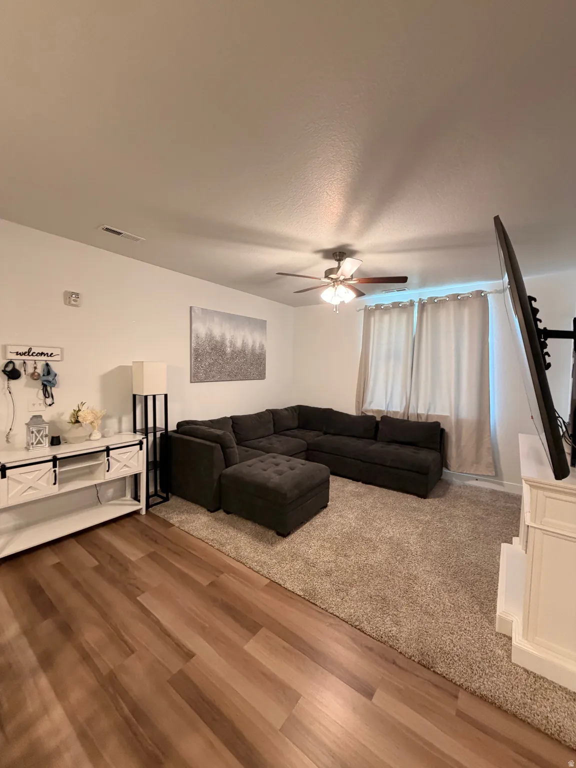 Spacious living area featuring wood-finish flooring, a ceiling fan with integrated lighting, and neutral wall tones