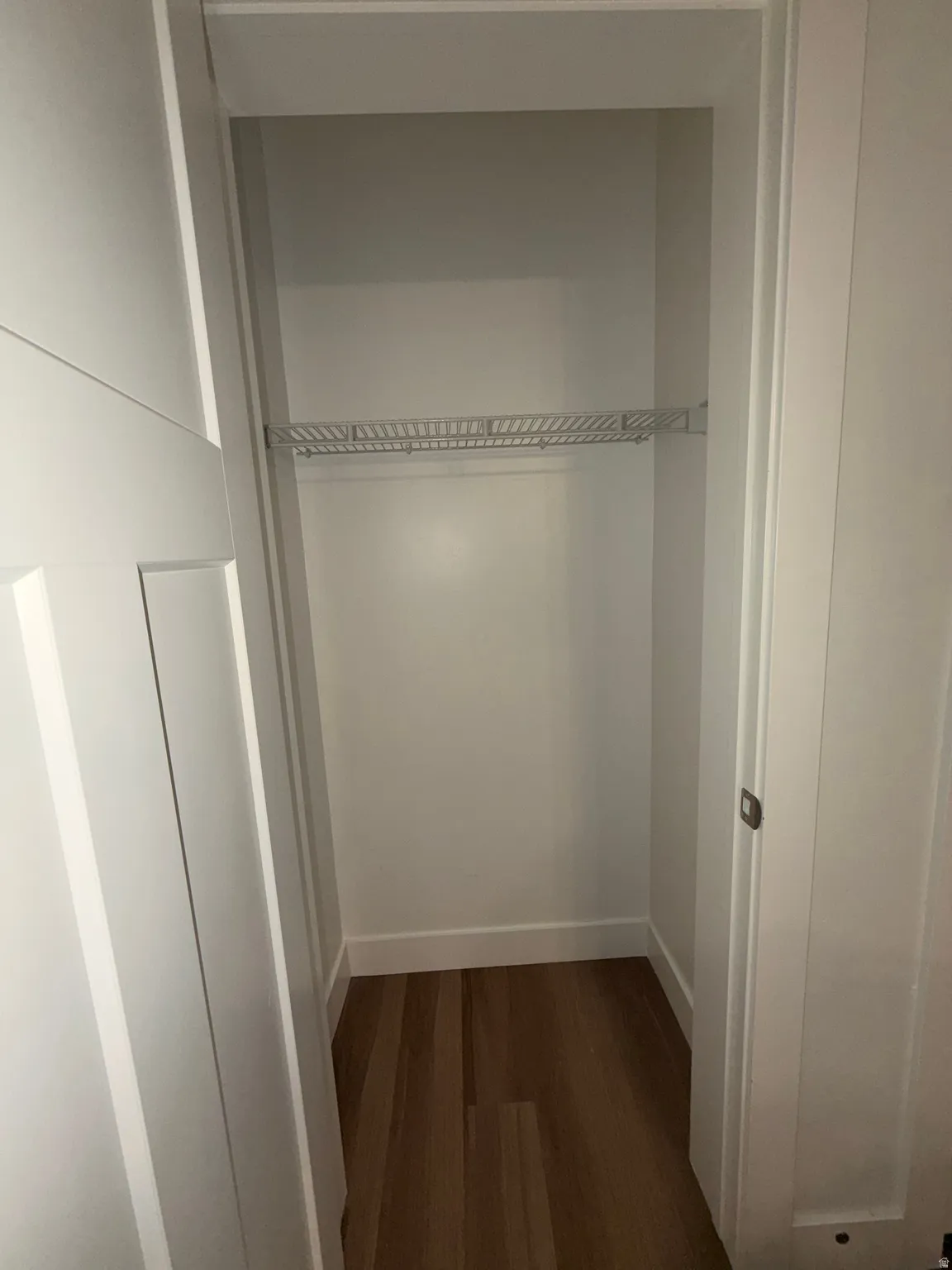 Recessed storage area featuring a wire shelf, wood-finish flooring, and white baseboards