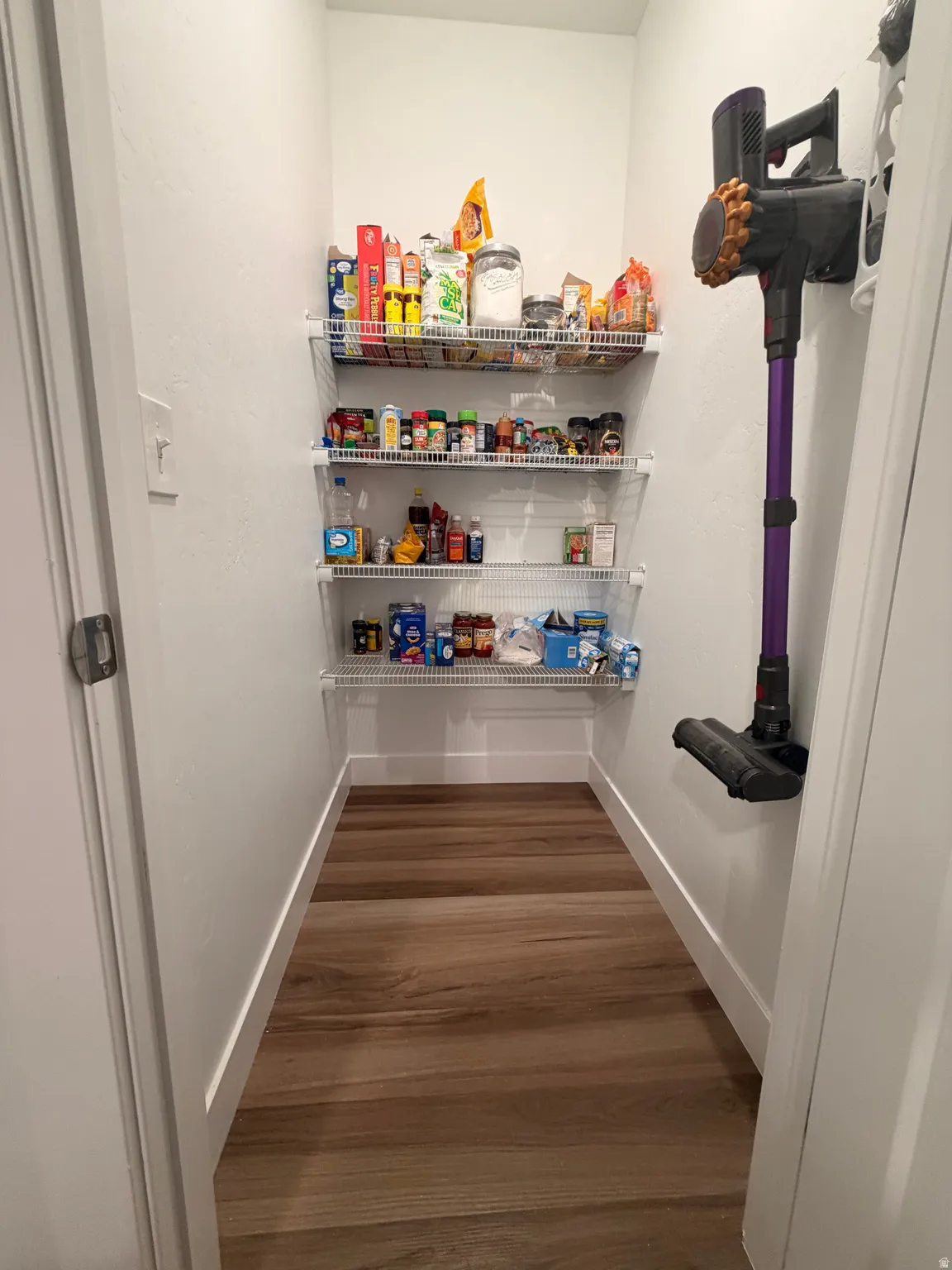 Walk-in pantry featuring multiple wire shelving units, wood-finish flooring, and white baseboards