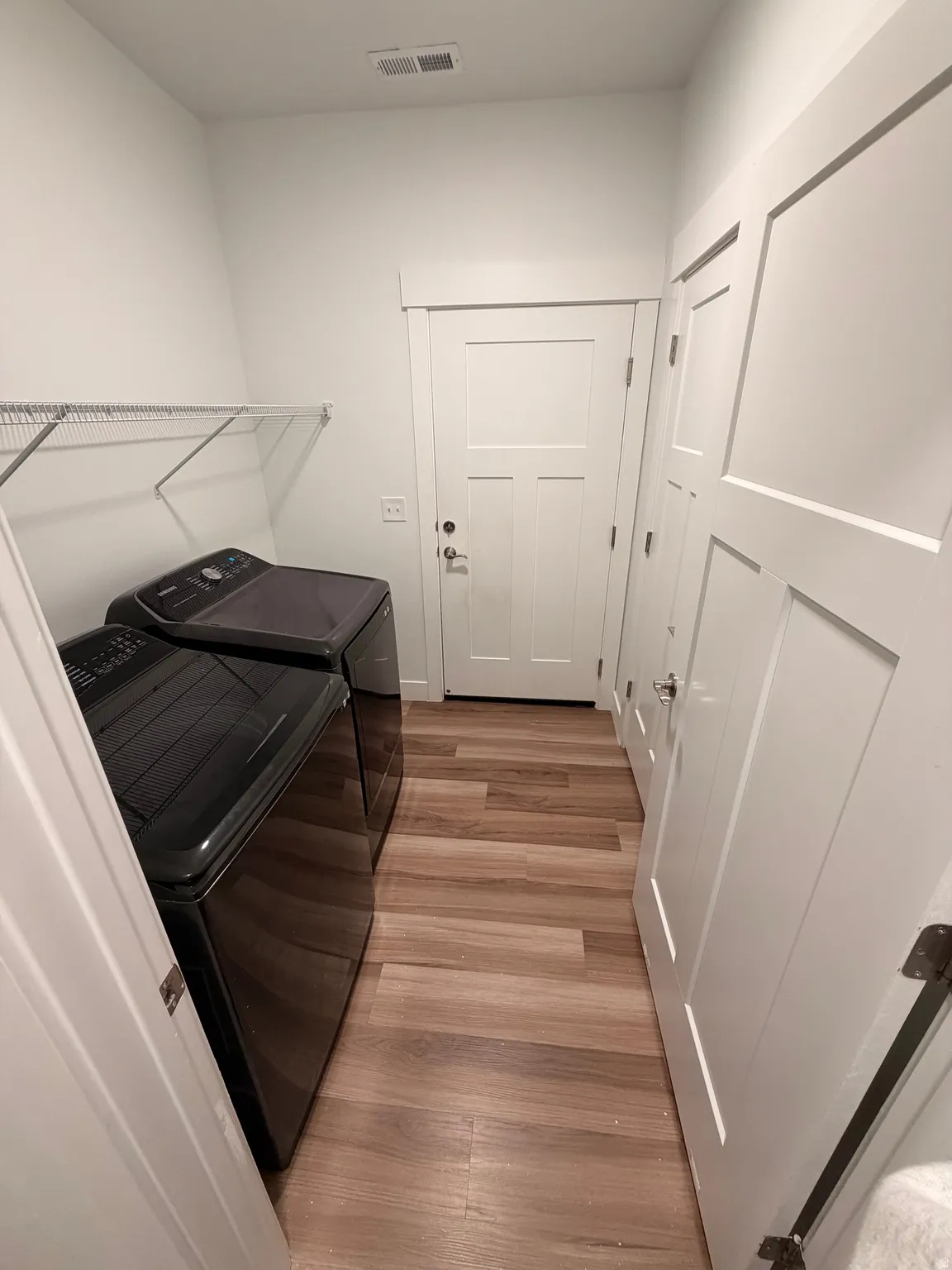Dedicated laundry area featuring wood-finish flooring, white walls, and a wire shelving unit