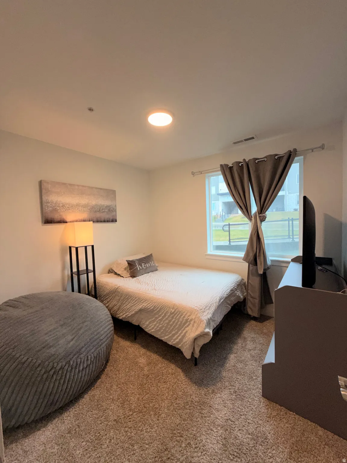 Bedroom featuring neutral carpeting, a large window with privacy curtains, a recessed ceiling light, and light-toned walls