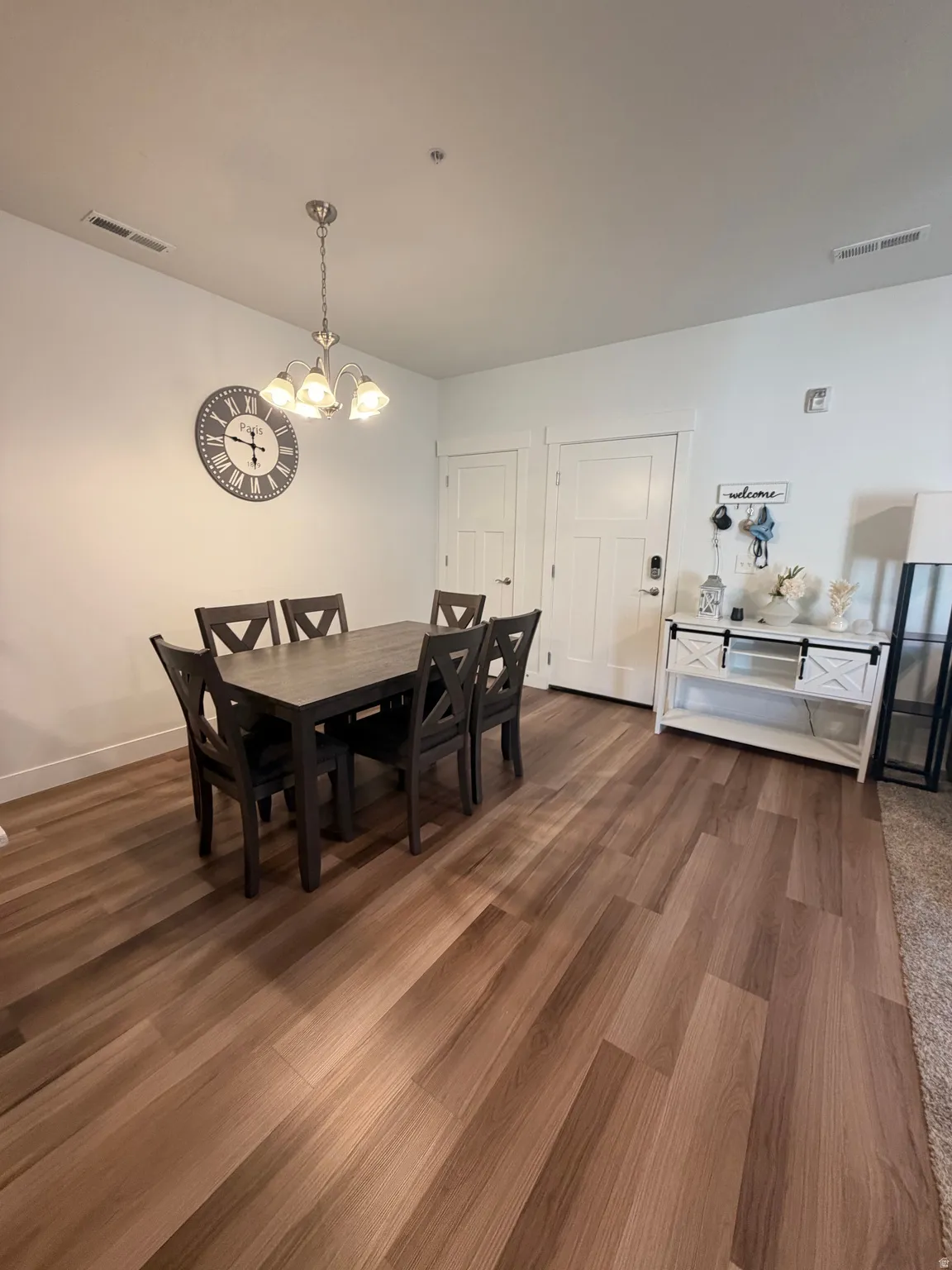 Spacious dining area featuring wood-finish flooring, a contemporary chandelier, white baseboards, and two paneled doors with white trim