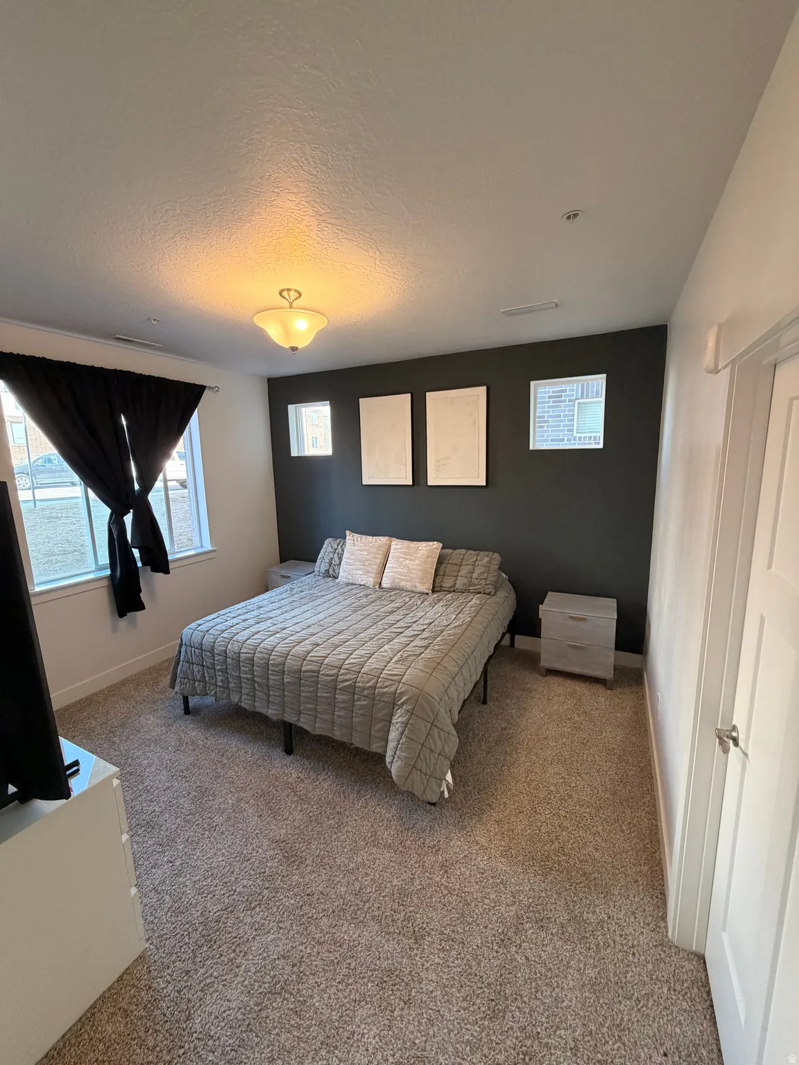 Spacious room featuring neutral carpeting, a dark accent wall, two window openings with black window treatments, and a ceiling-mounted light fixture