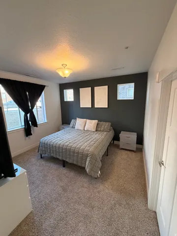 Spacious room featuring neutral carpeting, a dark accent wall, two window openings with black window treatments, and a ceiling-mounted light fixture