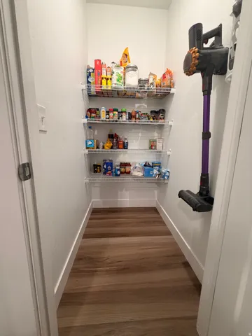 Walk-in pantry featuring multiple wire shelving units, wood-finish flooring, and white baseboards