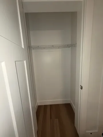 Recessed storage area featuring a wire shelf, wood-finish flooring, and white baseboards