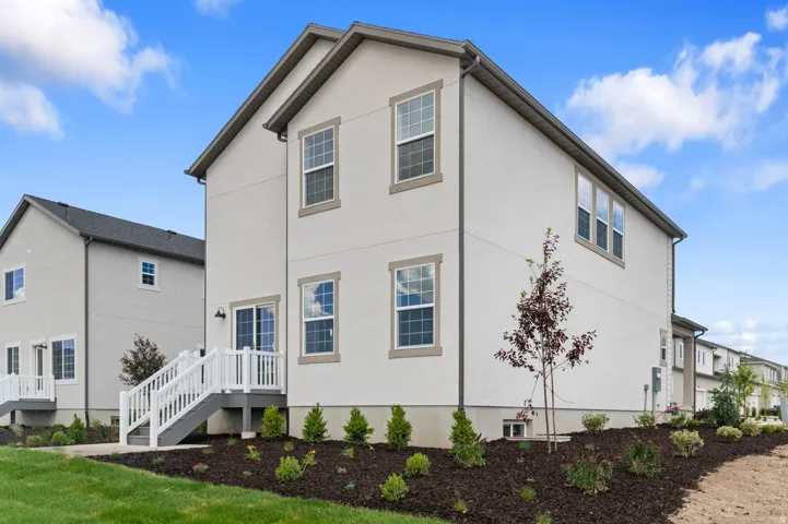 Rear exterior featuring stucco finish, multiple windows, and a sliding glass door leading to a white deck with stairs to grade