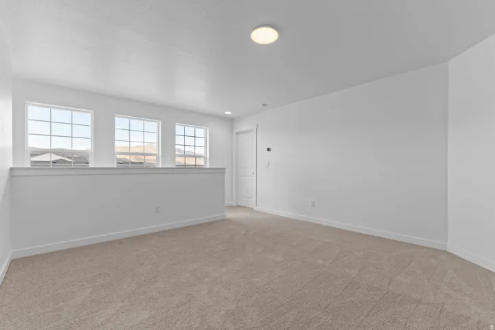 Carpeted loft space featuring three transom windows, a white half wall, a white interior door, and a flush-mount ceiling light
