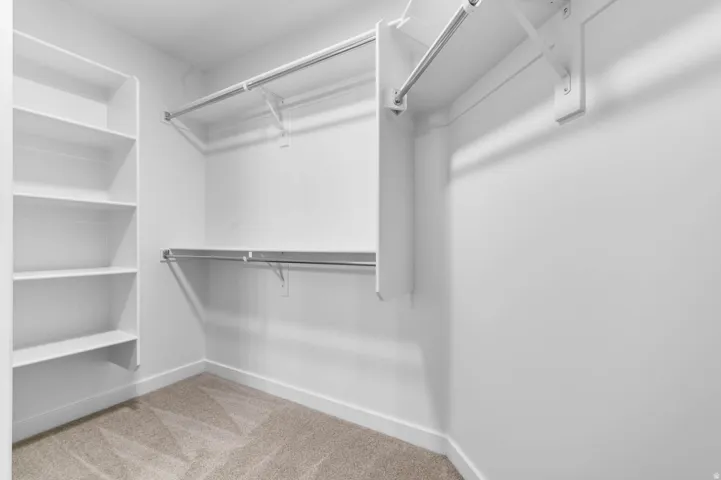 Walk-in closet featuring built-in shelving, two levels of hanging rods, and neutral carpet flooring