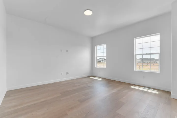 Spacious room featuring light wood-finish flooring, two large multi-pane windows, crisp white walls, and a recessed ceiling light