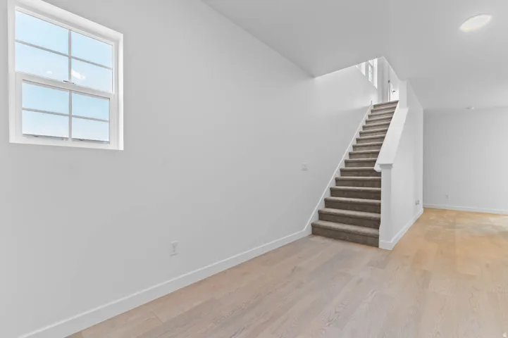 Open-concept space featuring light wood-finish flooring, white walls, and a staircase with carpeted treads